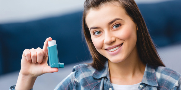 Person trägt ein kariertes Hemd und hält einen blauen Asthma-Inhalator in der rechten Hand.